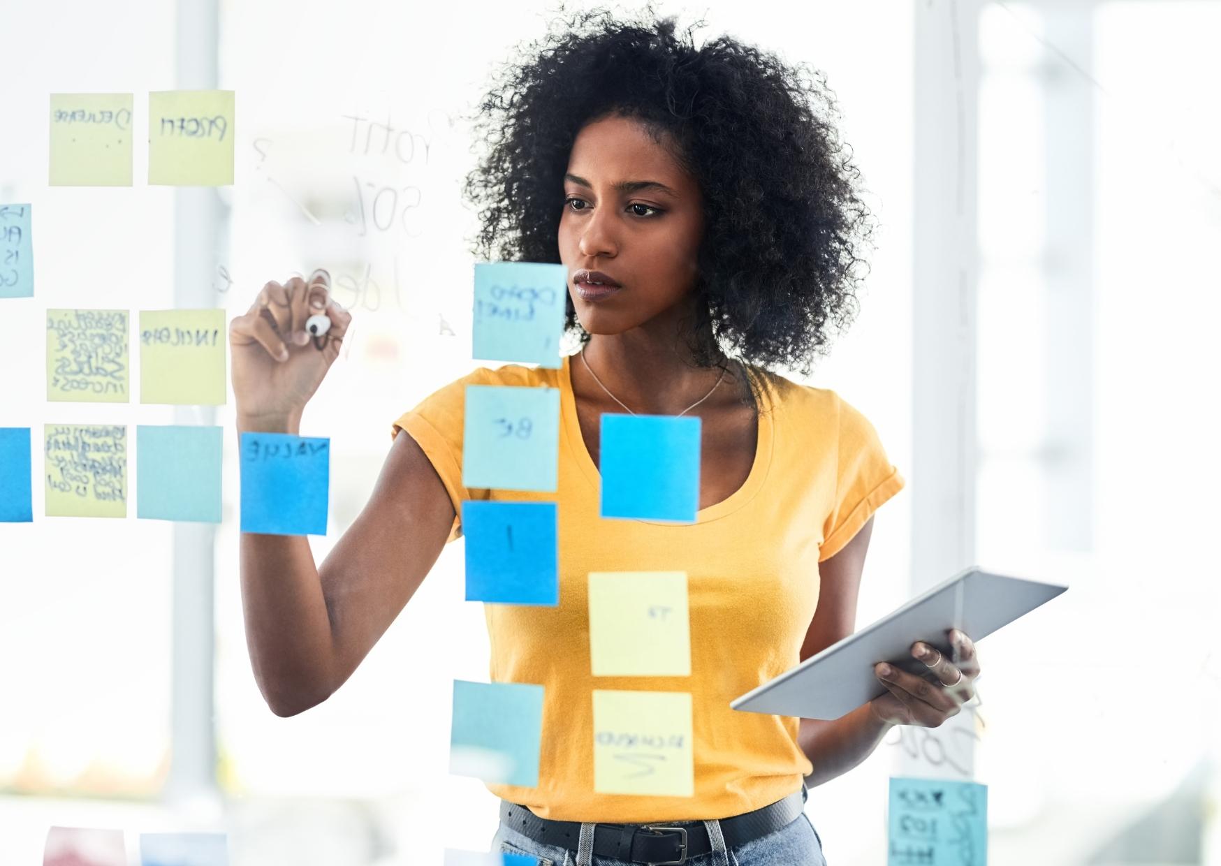 Vrouw die werkt aan SMART-doelstellingen van haar bedrijf Op de afbeelding zien we een vrouw die de SMART-doelstellingen van het komende jaar aan het opstellen is. Ze gebruikt post-its daarvoor.
